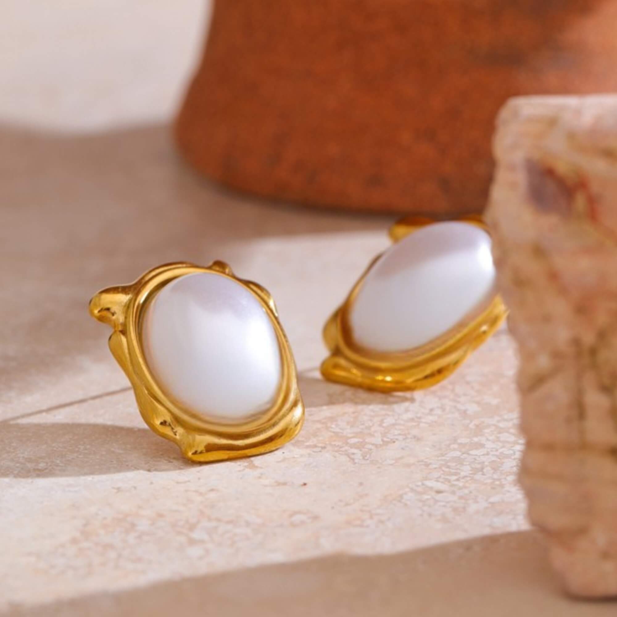 Gold earrings with white stones on a beige surface