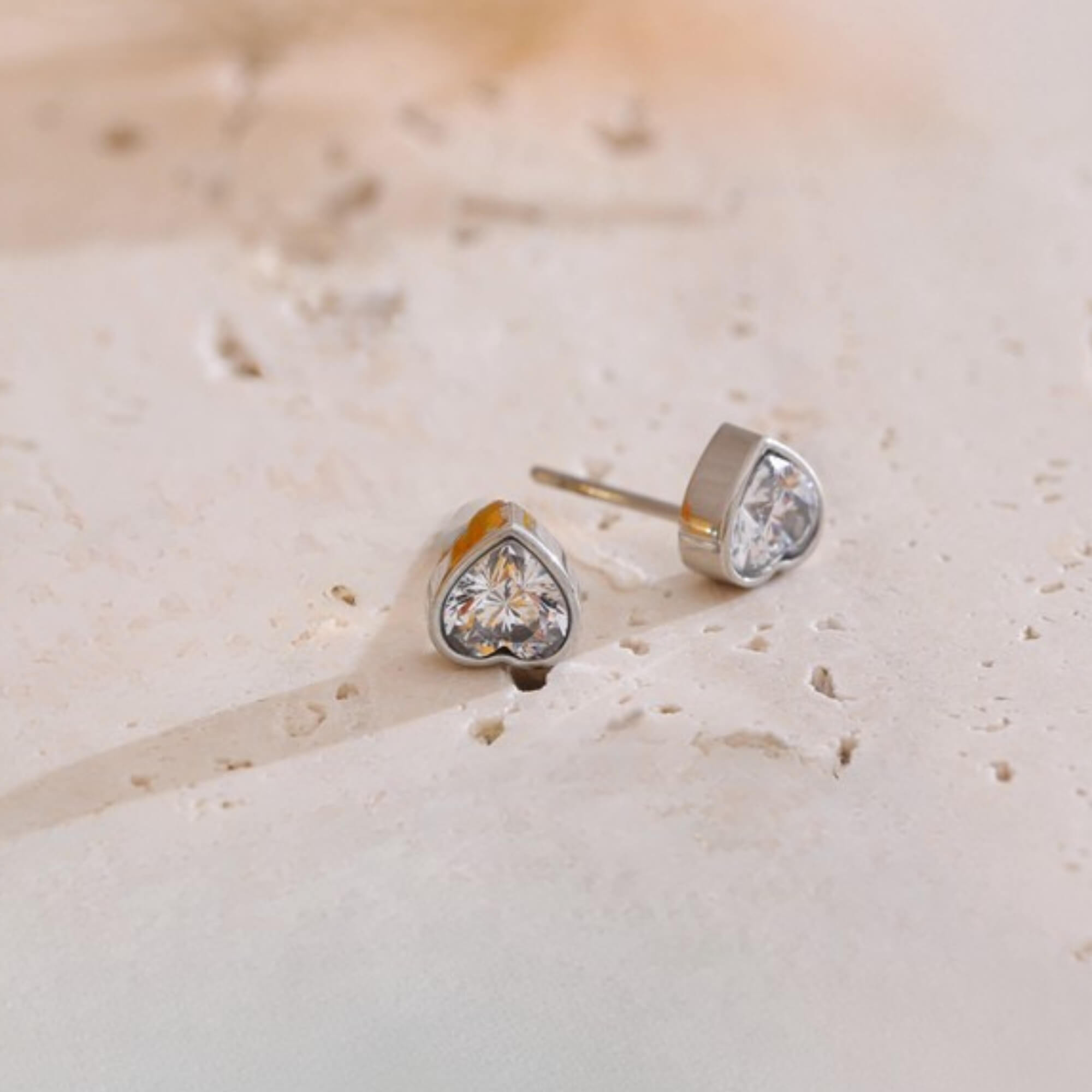 Heart-shaped crystal stud earrings on a light beige surface